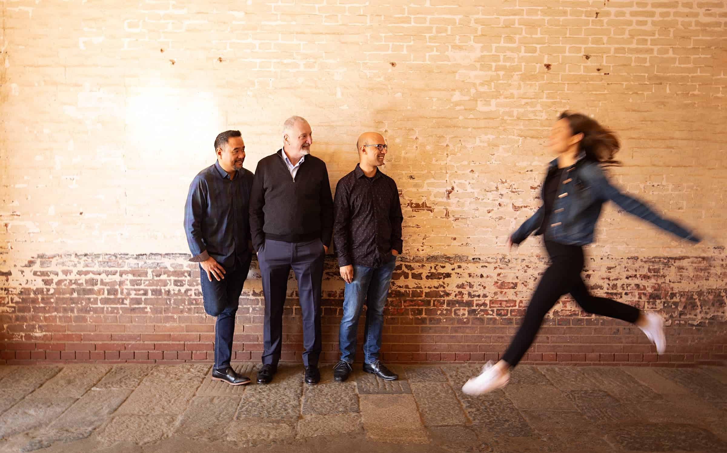 Yuna Lee Jumping into the frame with Zakarias Grafilo, Sandy Wilson, and David Samuel looking on against a wall